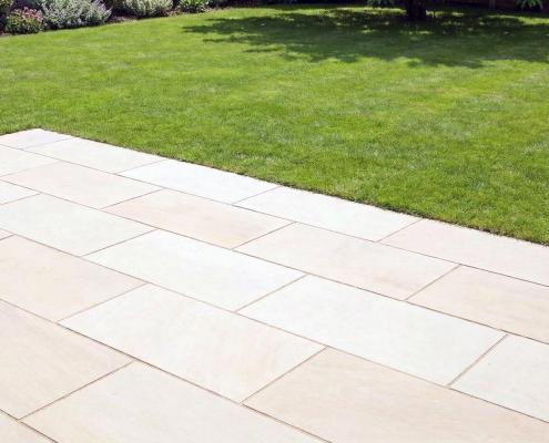 Eine Terrasse aus Feinsteinzeug in Sandstein-Optik in einem Garten mit gepflegter Rasenfläche