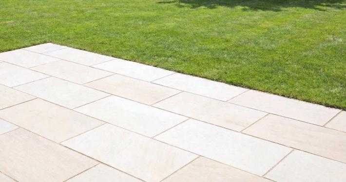 Eine Terrasse aus Feinsteinzeug in Sandstein-Optik in einem Garten mit gepflegter Rasenfläche